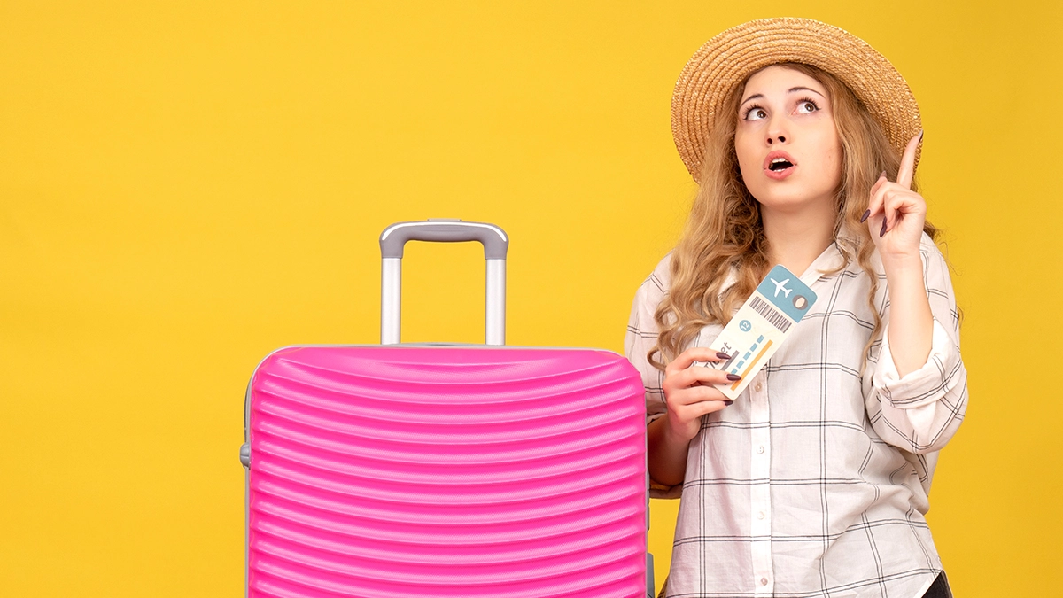 emotional young lady wearing hat showing ticket standing near her pink bag pointing up